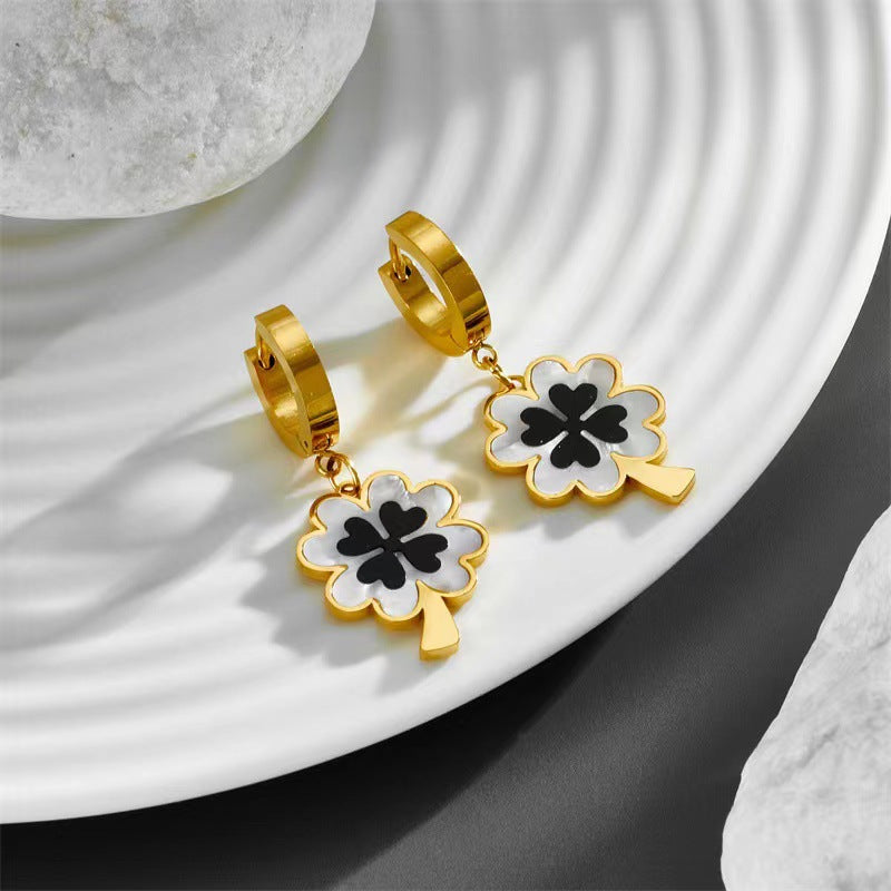 Gold hoop earrings with black and white clover-shaped charms on a white plate.