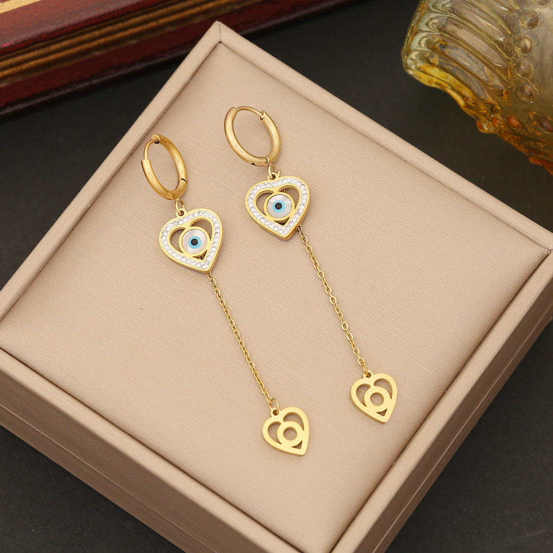 Gold heart-shaped earrings with a chain on a beige jewelry box.