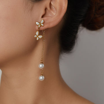 Butterfly-shaped earrings with pearl drops worn by a person against a neutral background