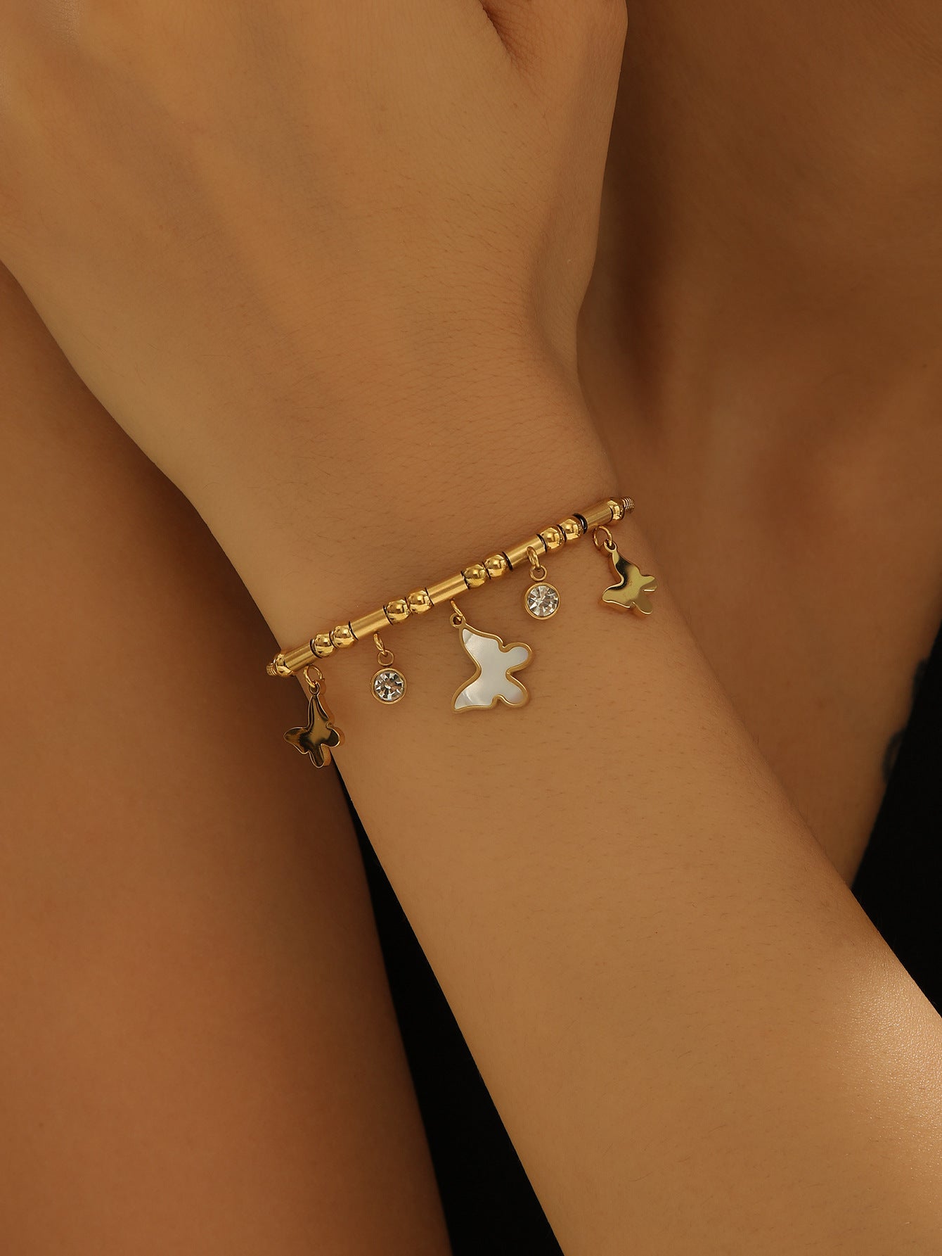 Gold bracelet with charms on a wrist against a brown background