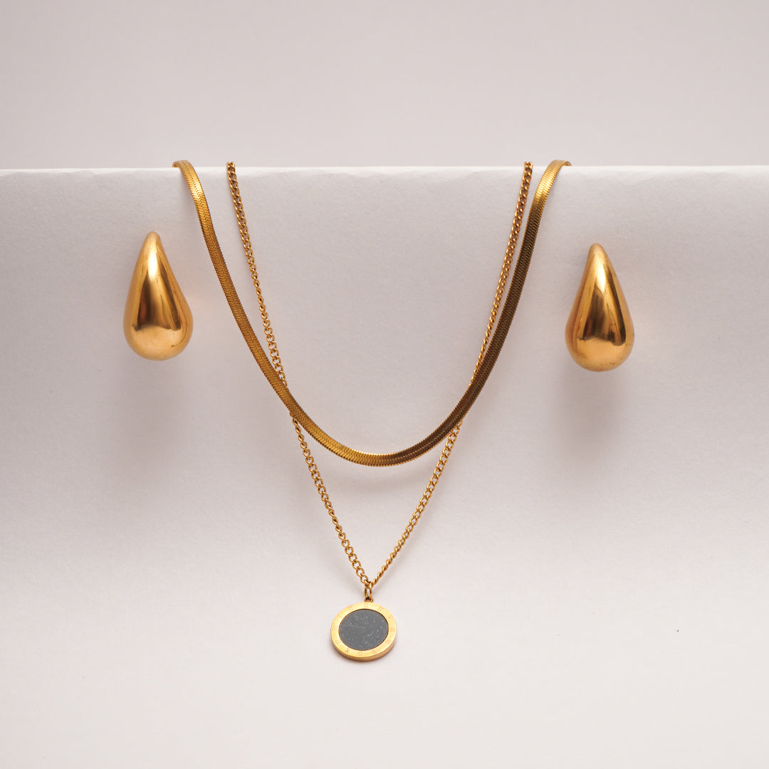 Gold necklace with a pendant and matching earrings on a white surface