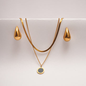 Gold necklace with a pendant and matching earrings on a white surface