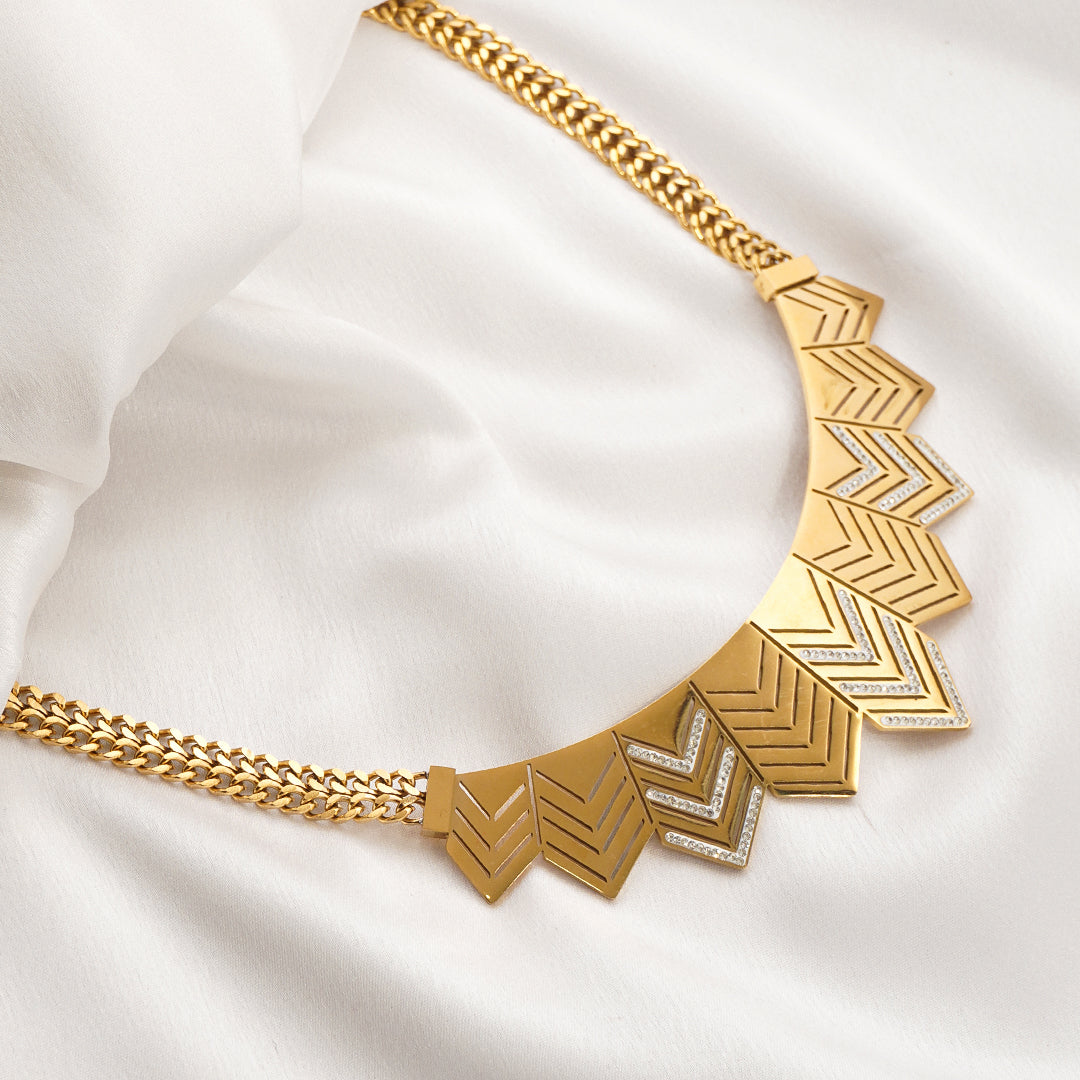 Gold necklace with geometric design on a white fabric background