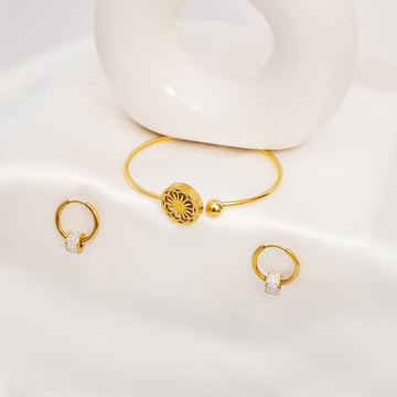 Gold bracelet and earrings on a white surface