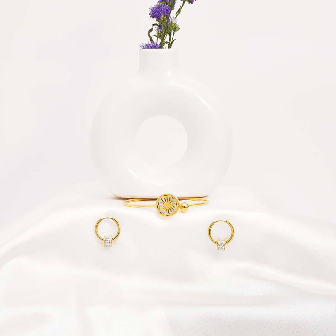 Gold jewelry set including a bracelet and two rings on a white surface with a small plant.