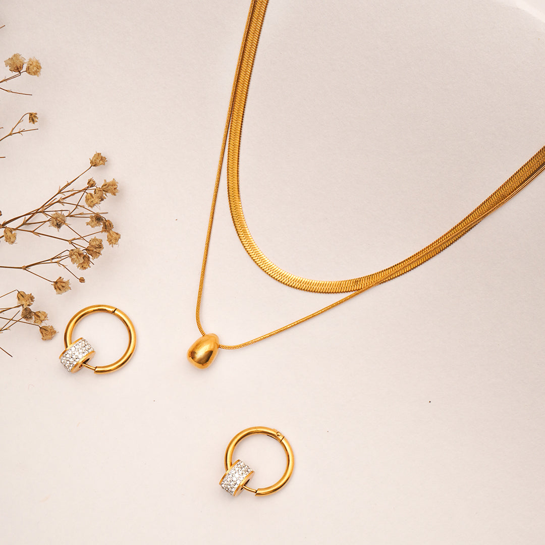 Gold necklace and earrings on a beige surface with dried flowers.