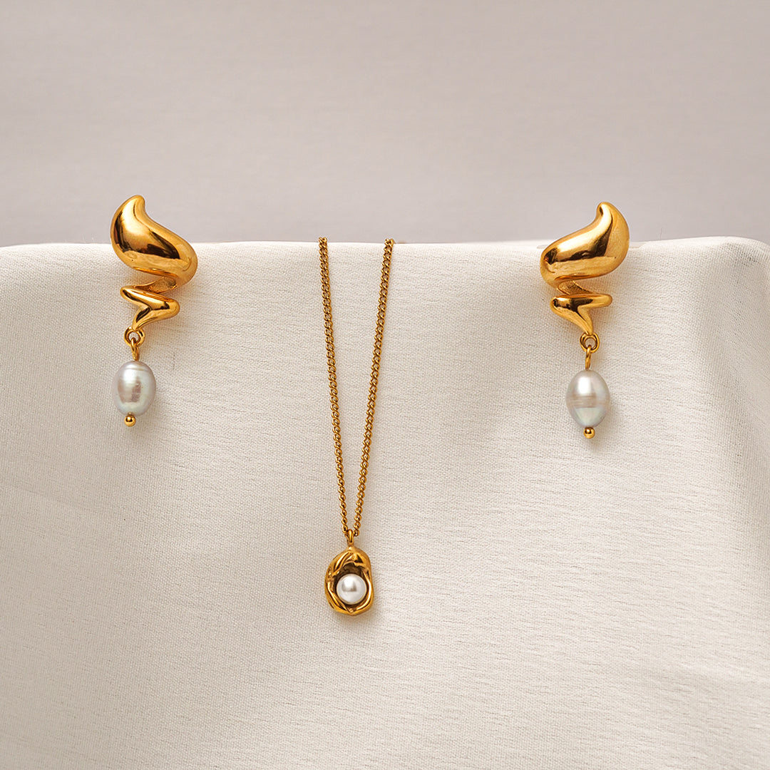 Gold earrings and necklace set on a beige surface