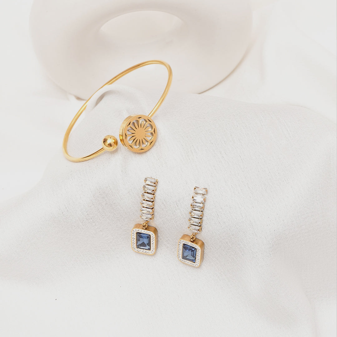 Gold bracelet and earrings with blue gemstones on a white background