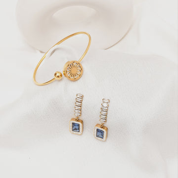 Gold bracelet and earrings with blue gemstones on a white background