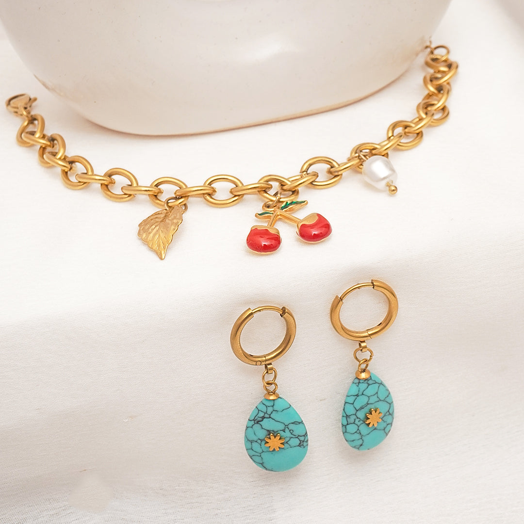 Gold bracelet with charms and turquoise earrings on a white background