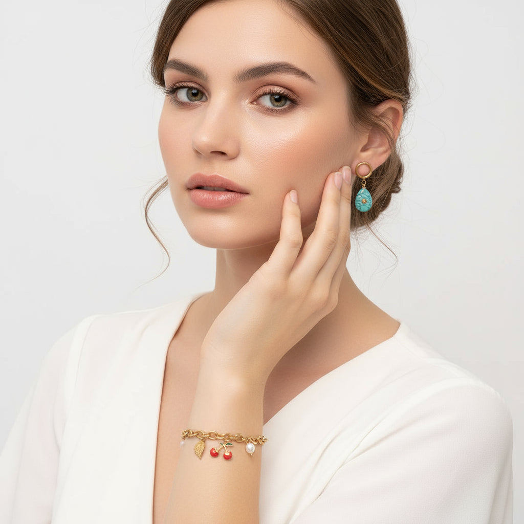 Gold bracelet with charms and turquoise earrings on a white background