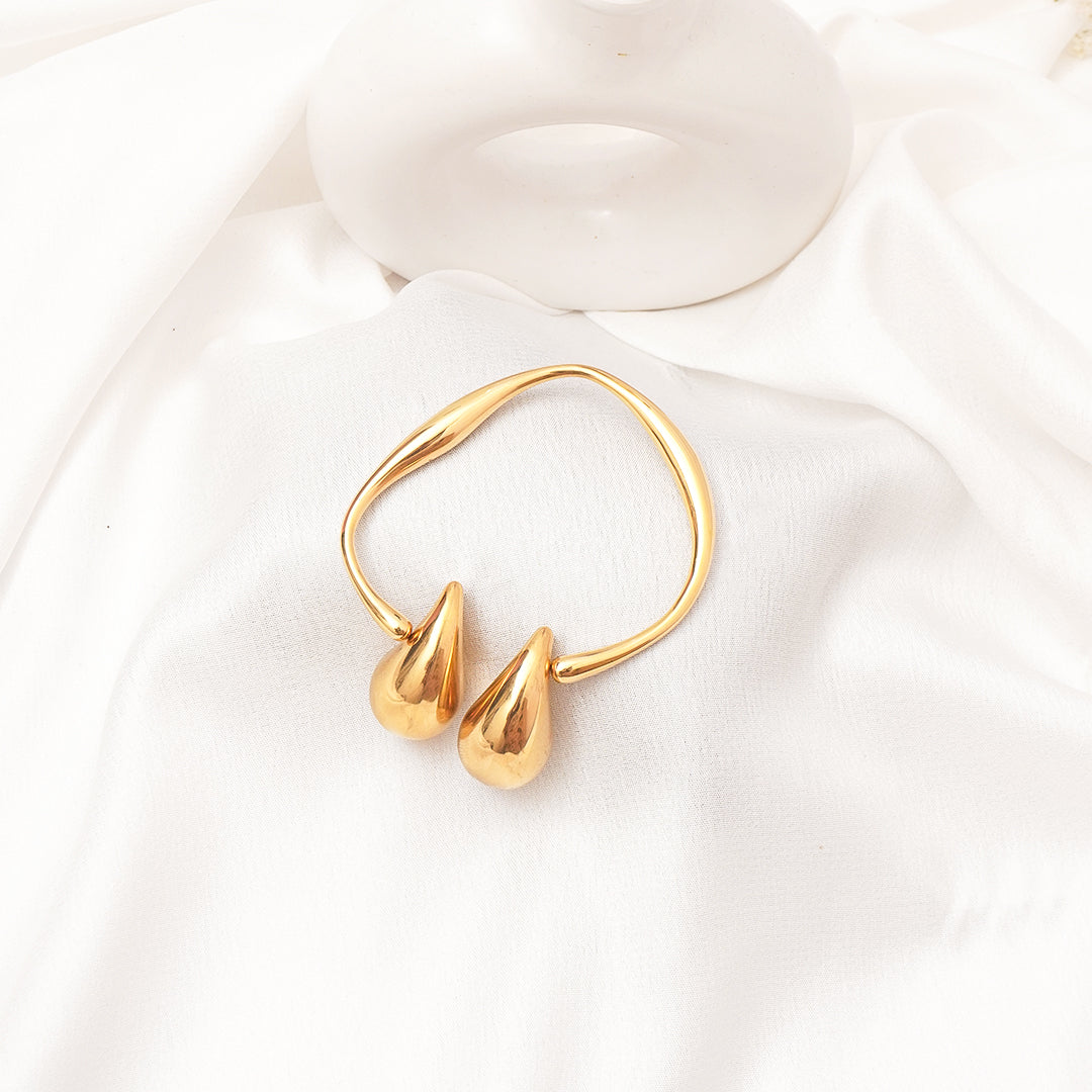 Gold bracelet with two droplet-shaped pendants on a white background