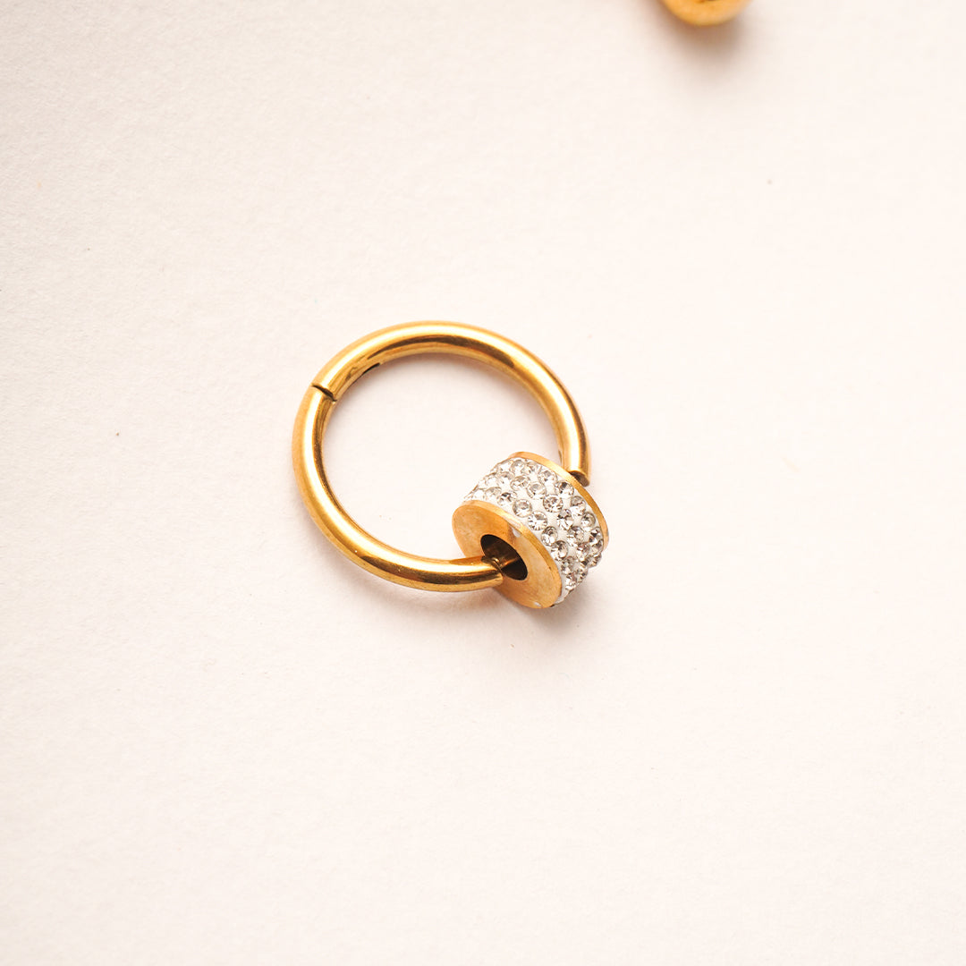 Gold hoop earring with a small round gemstone on a light beige background