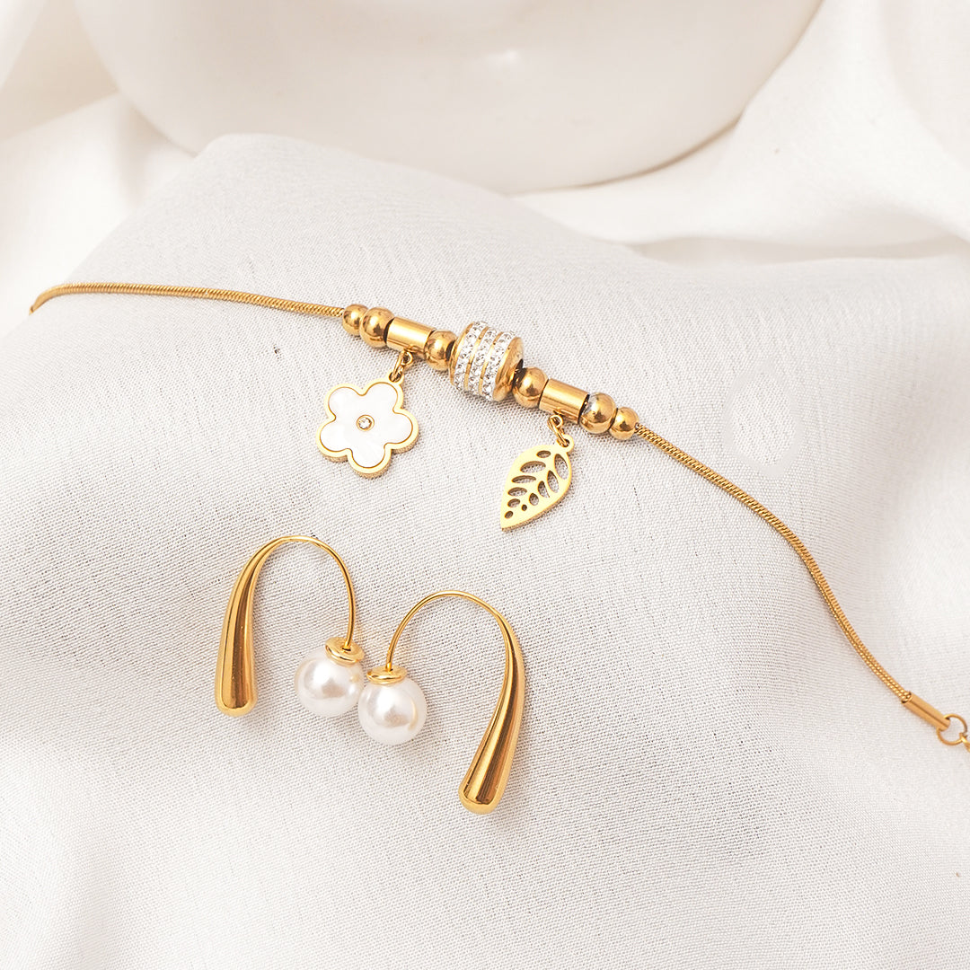 Gold necklace with floral and leaf charms and gold earrings on a white background