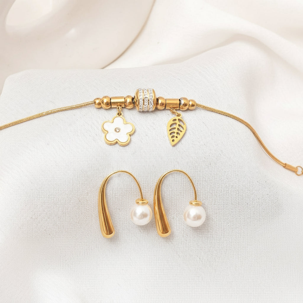 Gold necklace with charms and pearl earrings on a white fabric background