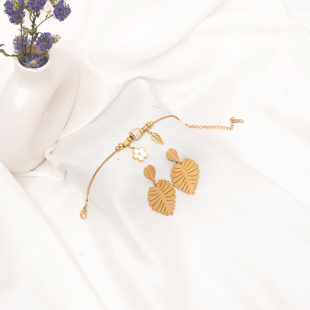 Gold earrings on a white surface with a small plant in the background