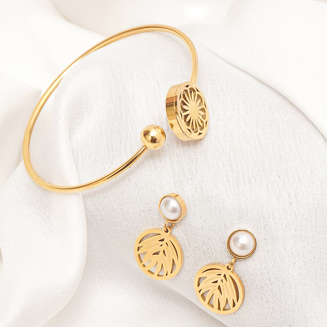 Gold bracelet and earrings with pearl accents on a white fabric background