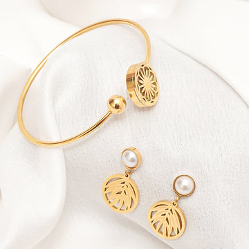 Gold bracelet and earrings with pearl accents on a white fabric background