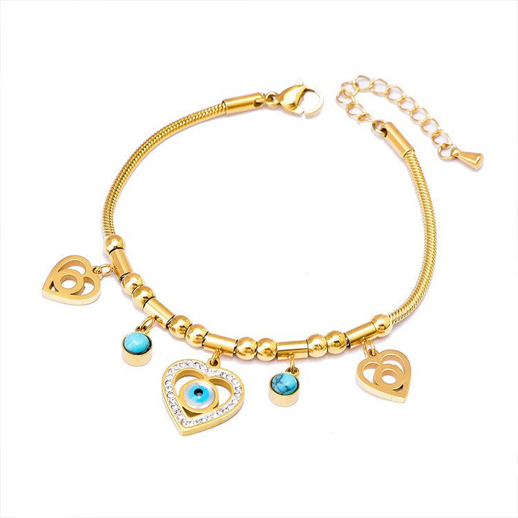Gold bracelet with heart and eye charms on a white background