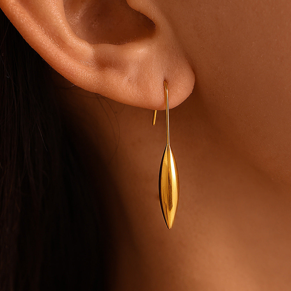 Gold earrings with a white bowl, fig, and flowers on a textured surface
