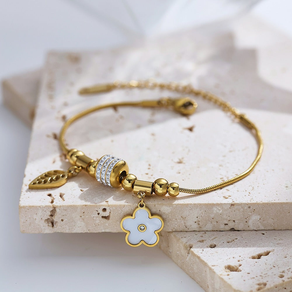 Gold bracelet with floral charm on a stone surface