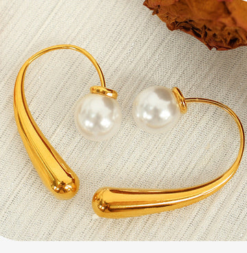 Gold hoop earrings with pearl-like beads on a textured beige surface