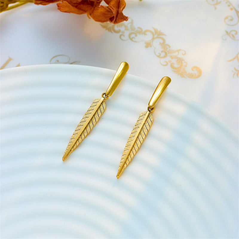 Gold feather-shaped earrings on a light blue plate with floral background