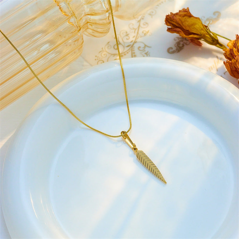 Gold necklace with a leaf pendant on a white plate with dried flowers and a fan in the background