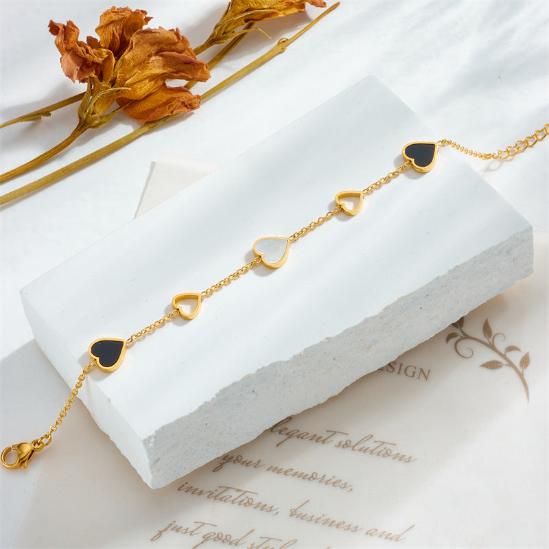 Gold necklace with black heart charms on a white stand with dried flowers.