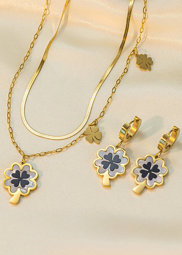 Gold necklace and earrings with clover designs on a beige background