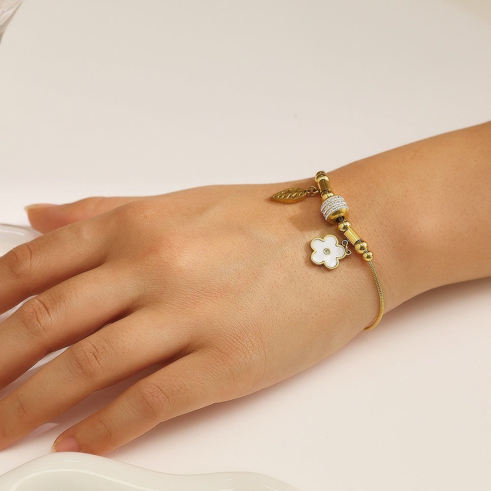Gold bracelet with a white flower charm on a wrist against a light background