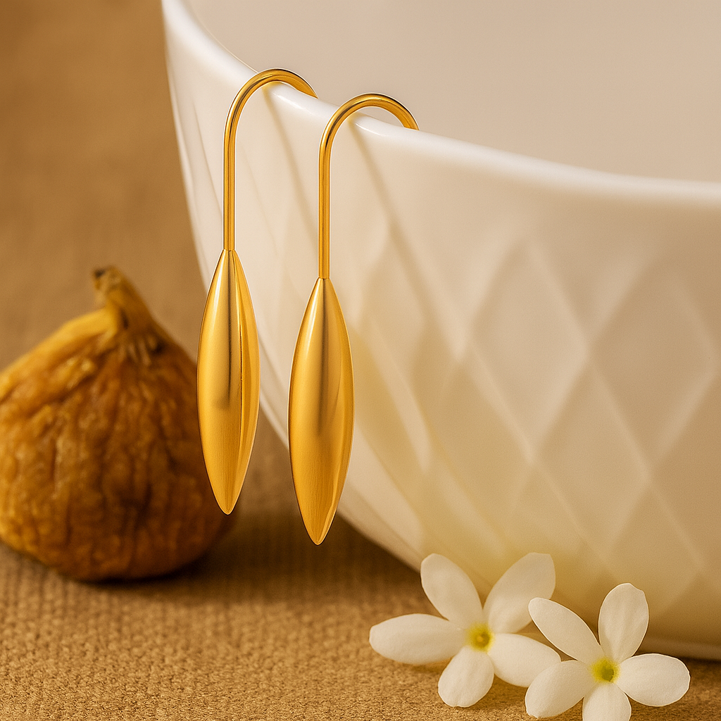 Gold earrings with a white bowl, fig, and flowers on a textured surface