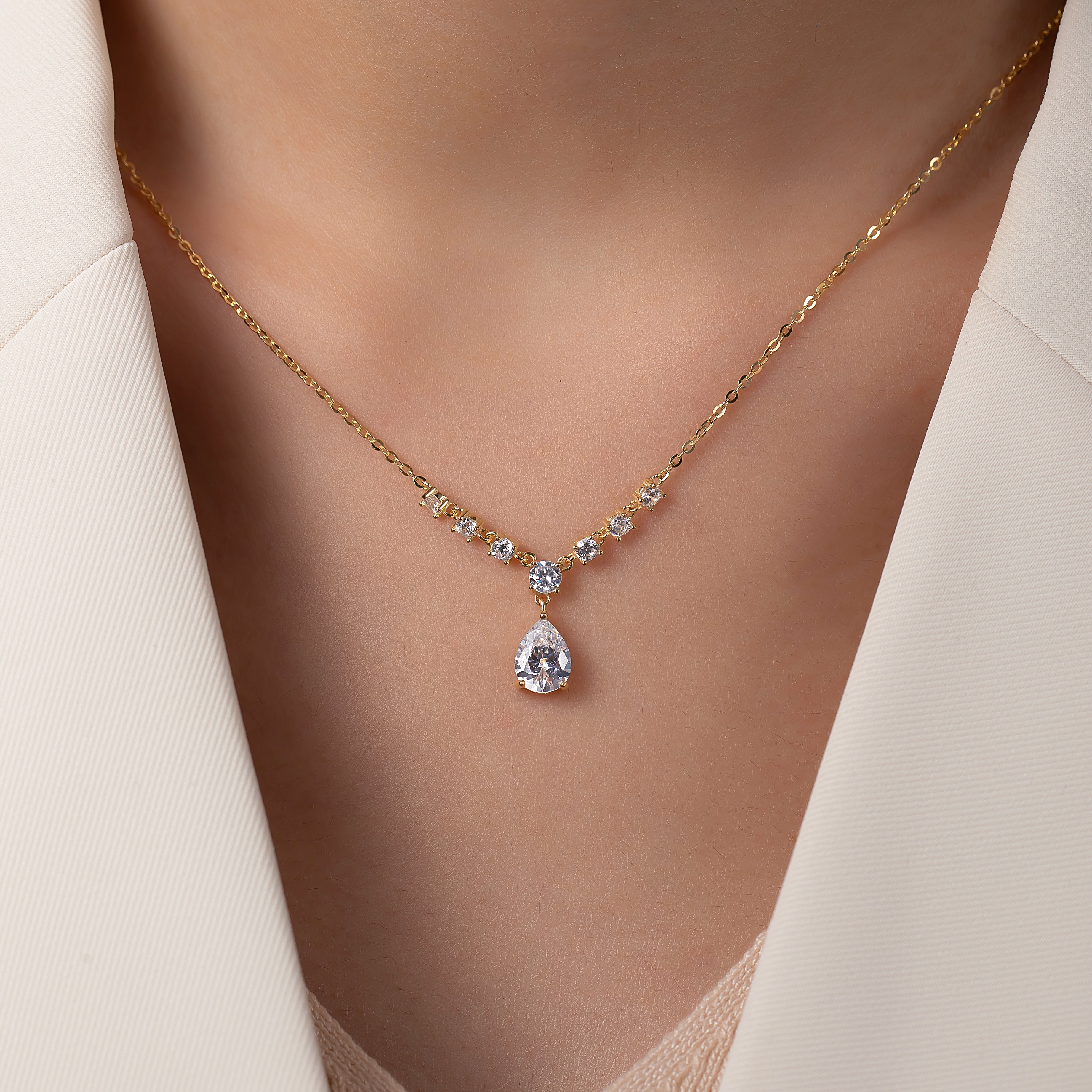 Gold necklace with a teardrop-shaped pendant on a blurred background