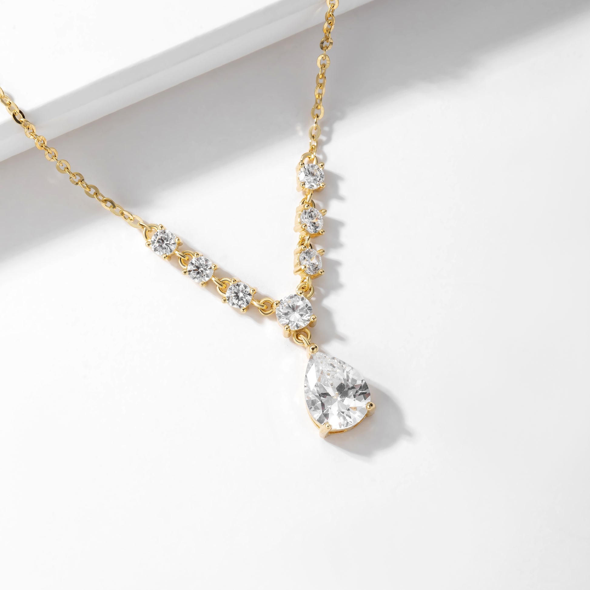 Gold necklace with clear teardrop pendant on a white background