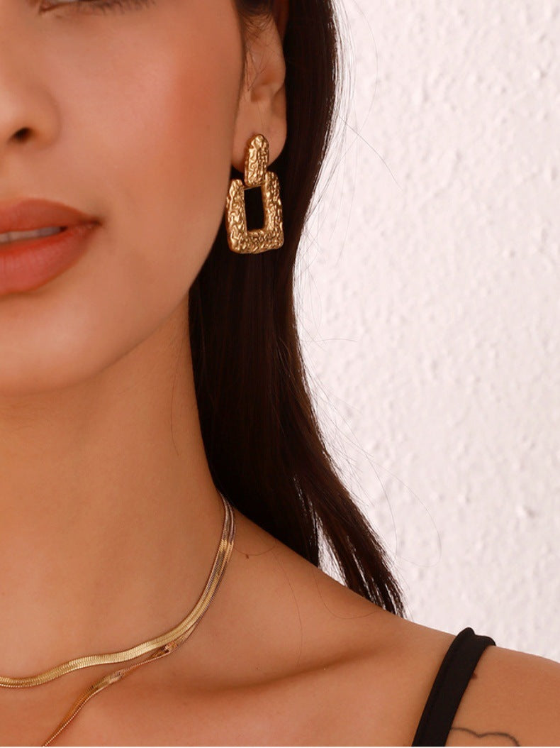 Close-up of a woman wearing gold hoop earrings with a neutral background
