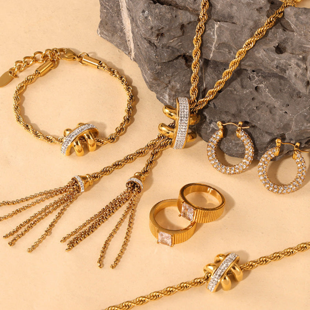 Gold jewelry set including necklace, bracelet, rings, and earrings on a stone surface.