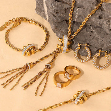 Gold jewelry set including necklace, bracelet, rings, and earrings on a stone surface.