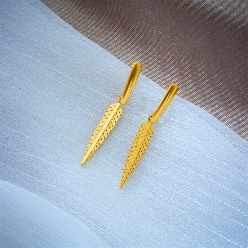 Gold leaf-shaped earrings on a textured fabric background