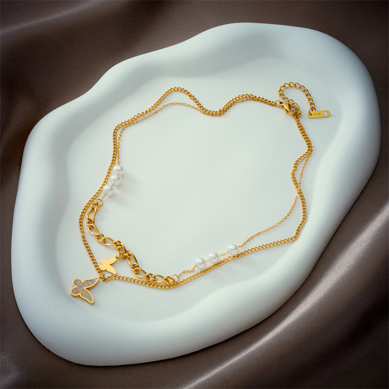 Gold necklace with heart and butterfly charms on a white stone surface