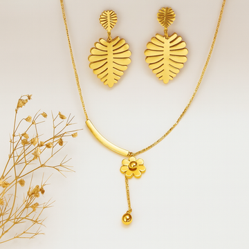 Gold necklace and earrings with a floral pendant on a light background