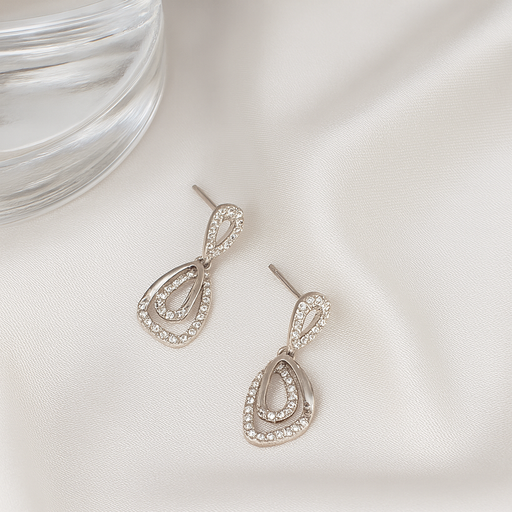 Silver teardrop earrings with clear stones on a white satin surface.