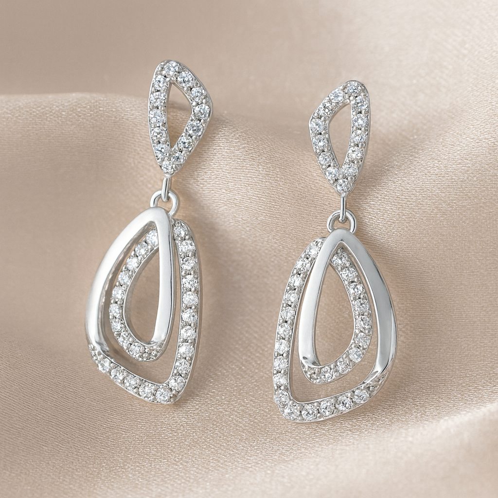 Silver teardrop earrings with clear stones on a beige satin background