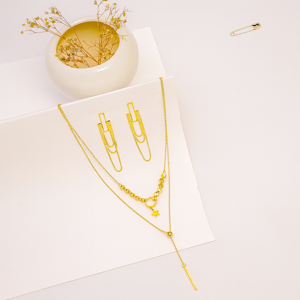 Gold necklaces on a white surface with a small decorative bowl and safety pin.