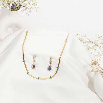 Gold necklace and earrings with gemstones on a white fabric background
