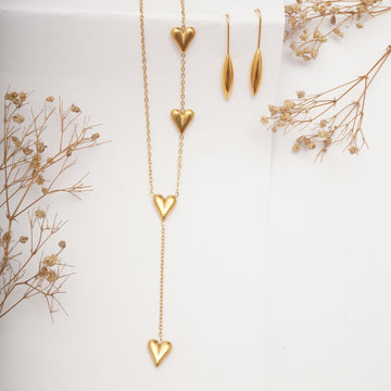 Gold necklace with heart-shaped pendants on a white background with dried flowers.