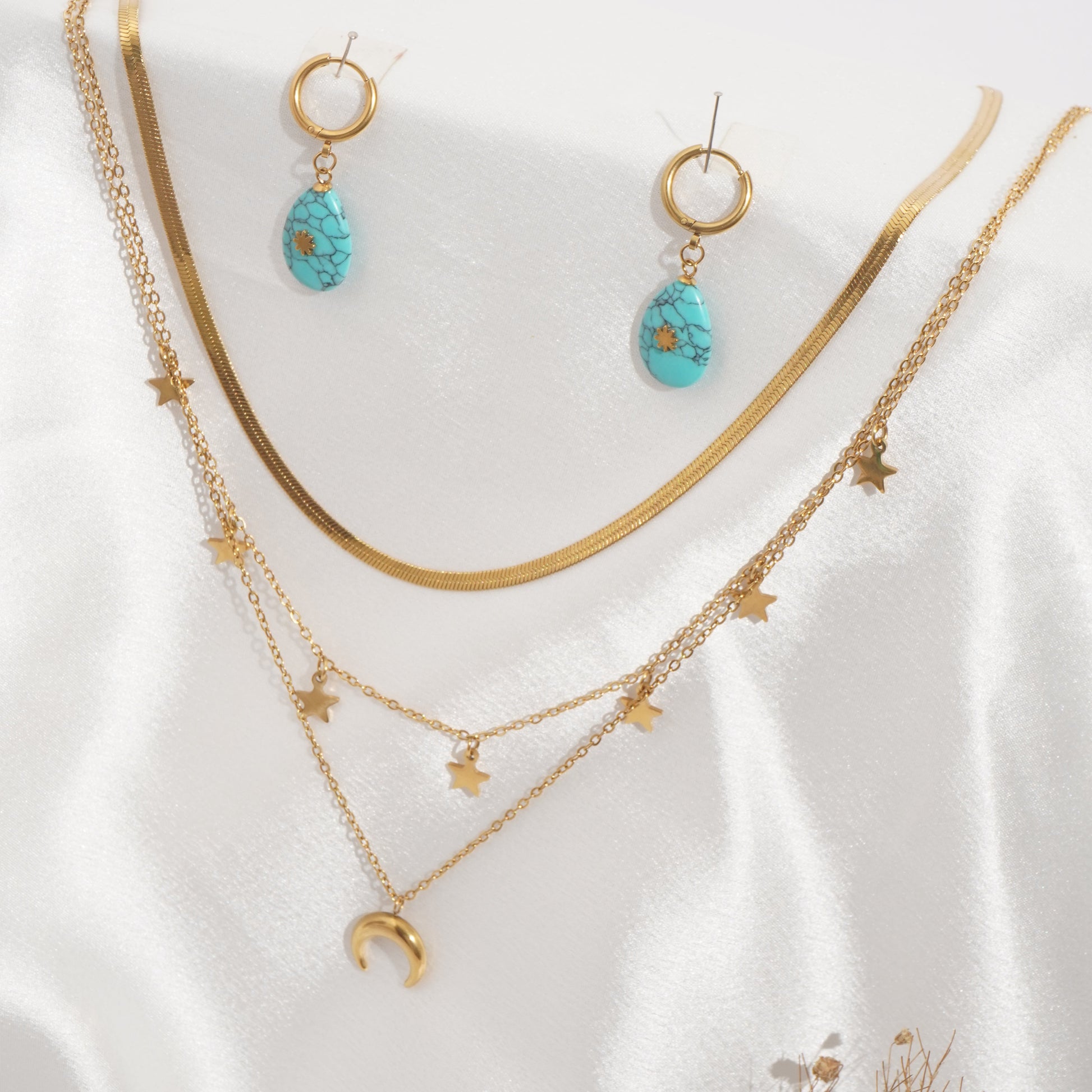 Gold jewelry set with turquoise stones on a white fabric background