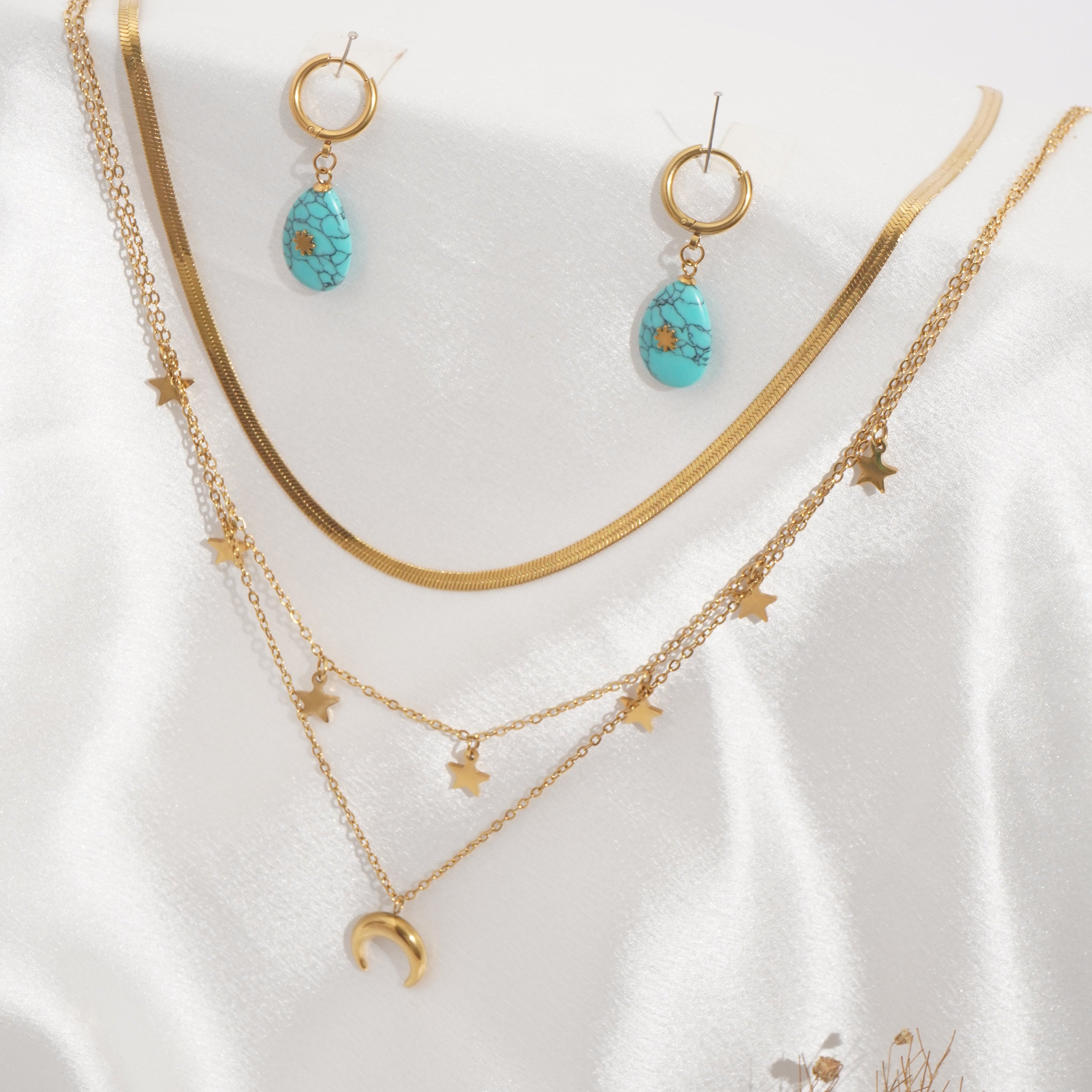 Gold jewelry set with turquoise stones on a white fabric background