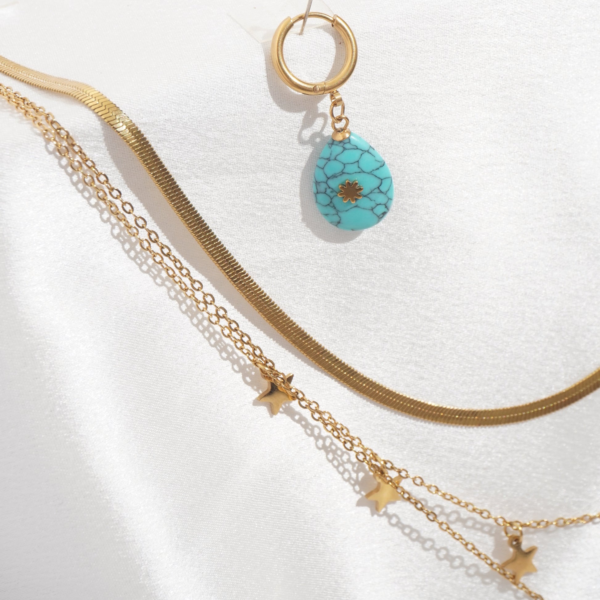 Gold necklace with star and turquoise pendant on a white background