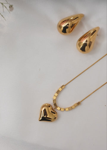 Gold heart-shaped necklace and teardrop-shaped earrings on a white background with small flowers.
