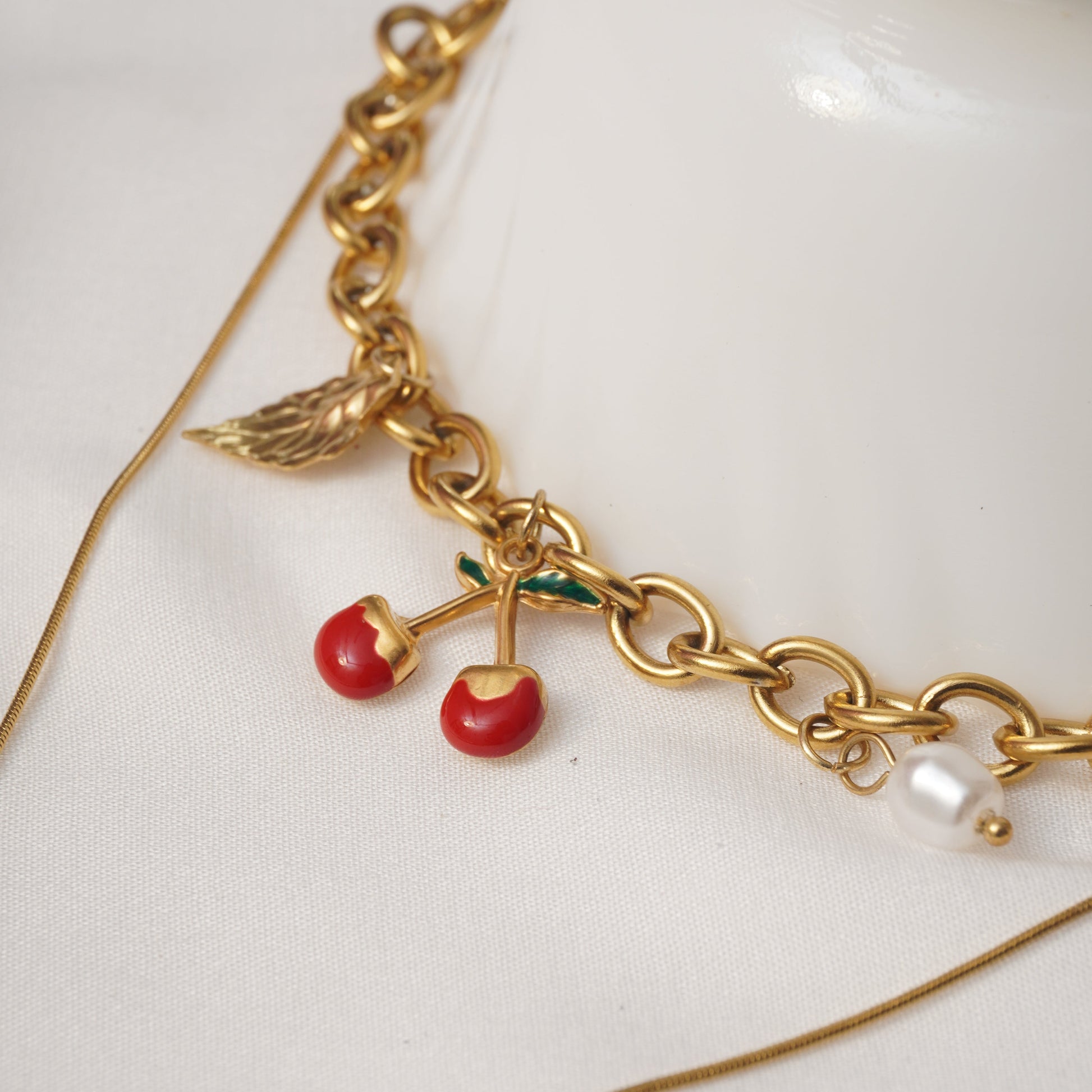 Gold bracelet with red berries and green leaves on a white surface